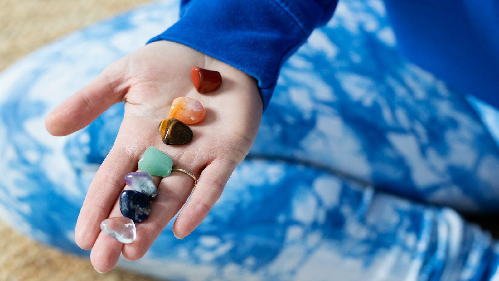 Hand holding colorful chakra healing stones for a spiritual clothing guide about dressing with intention