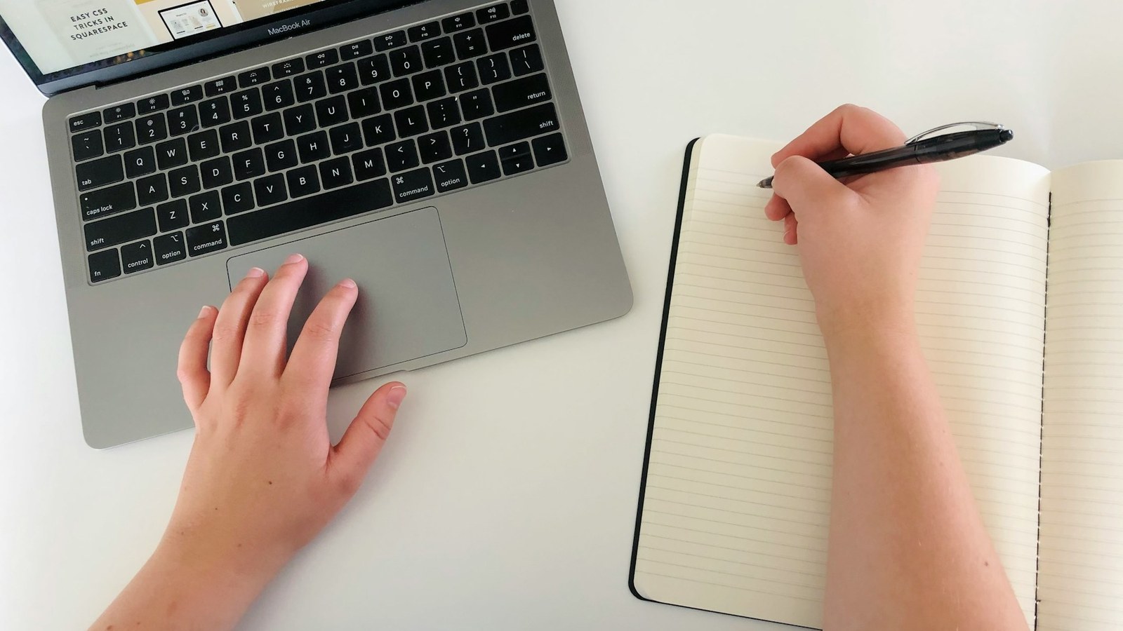 Person writing in a notebook beside a laptop for shadow work prompts for activists and conscious creatives